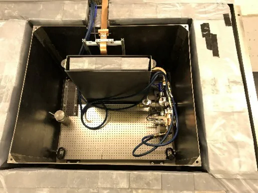 Looking down into the open lead enclosure at CERF-NM: a black-walled box with the cavity and waveguide parts on a breadboard, cables and a copper waveguide coming in from the top.